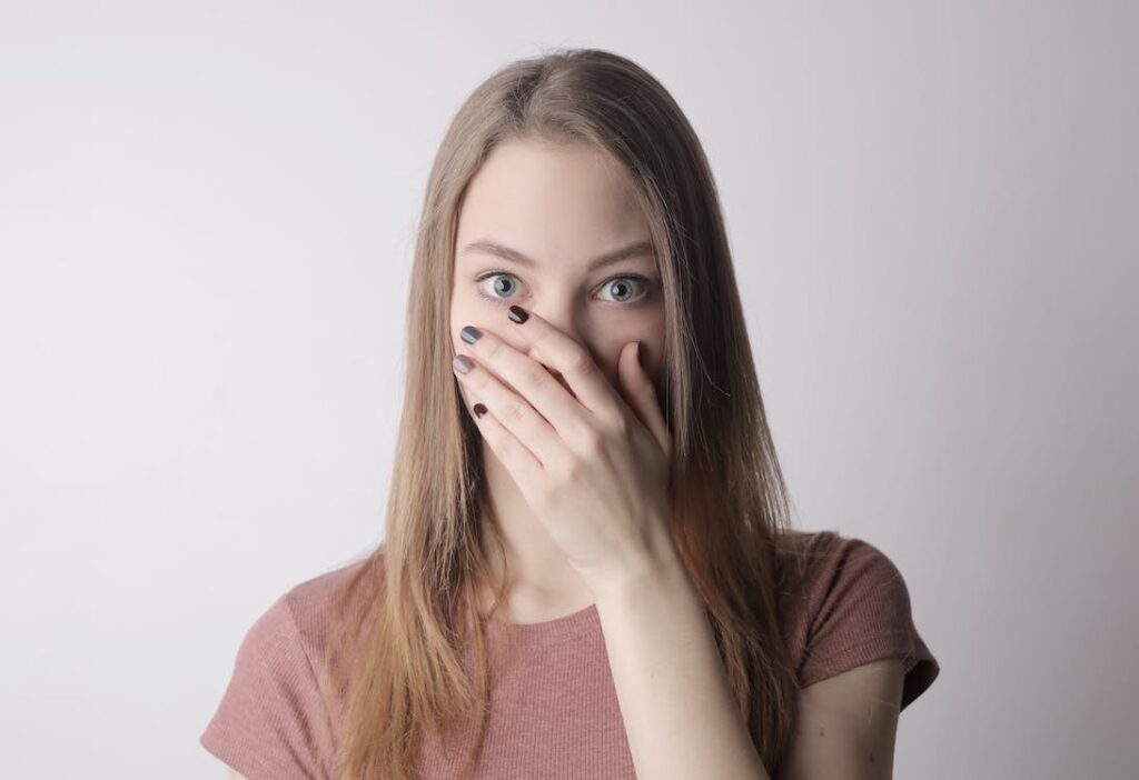 秘密を保ちながら口を覆っているカジュアルな服装の若い驚く女性関連の無料ストックフォト